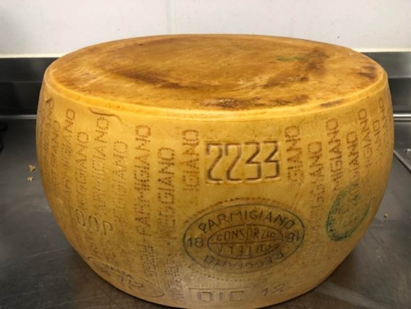 Closeup of a man slicing a Parmigiano Reggiano cheese wheel Stock