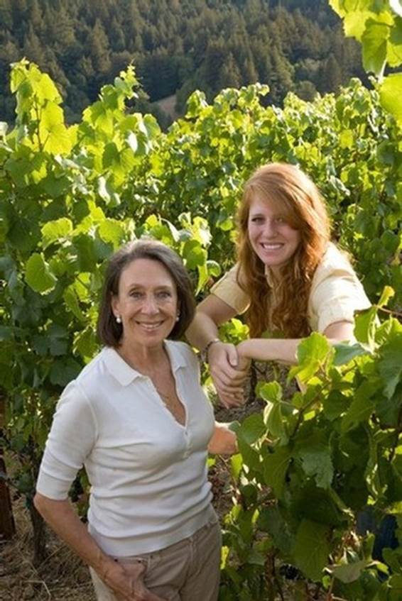 A person and a young person standing in a vineyard  Description automatically generated