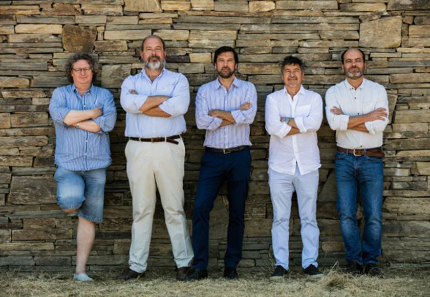 A group of men standing in front of a stone wall  Description automatically generated